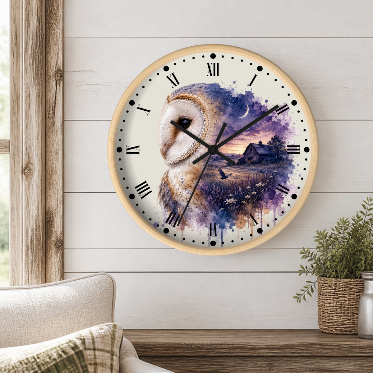 A round wall clock with a light wood frame hangs on a white shiplap wall above a wooden table. The clock face features a watercolor-style illustration of a barn owl over a purple and blue sunset landscape with a small cabin and moon.