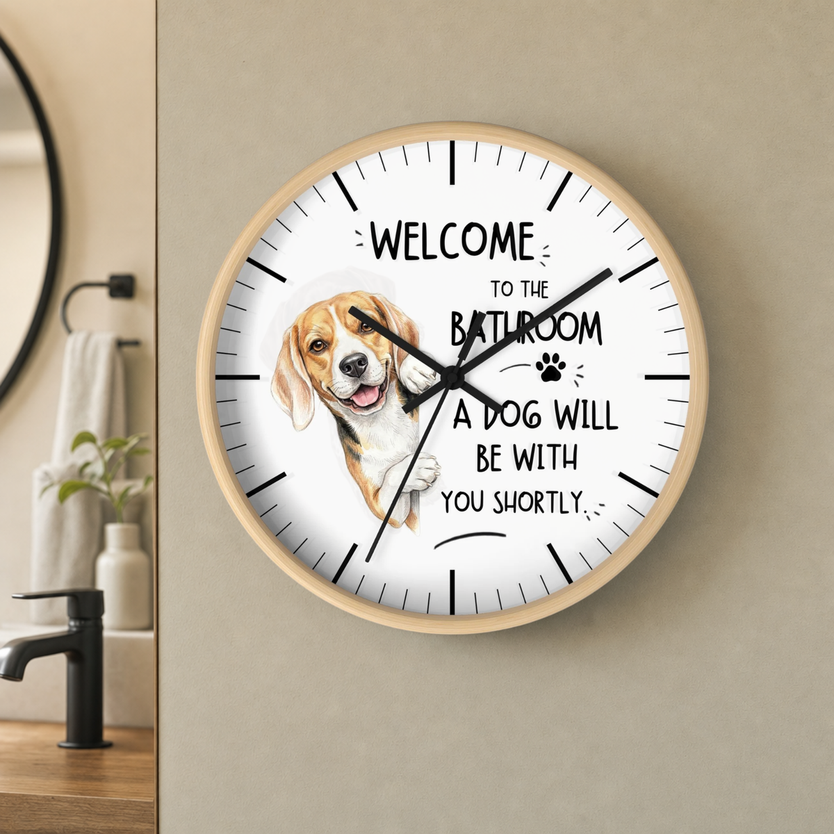 A round wall clock with a light wood frame hangs on a beige wall in a bathroom setting. The clock face is white with black text reading 'WELCOME TO THE BATHROOM A DOG WILL BE WITH YOU SHORTLY' and a painted beagle illustration replacing the center hour markers.