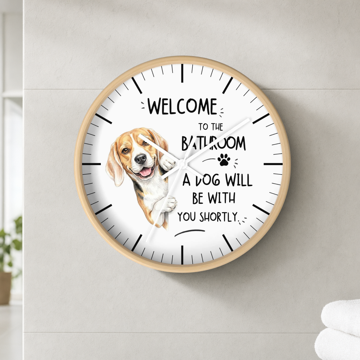 A round wall clock with a light wood frame and a white face, mounted on a light gray tiled wall. The clock features a watercolor illustration of a beagle and the text 'WELCOME TO THE BATHROOM A DOG WILL BE WITH YOU SHORTLY' with a small paw print.