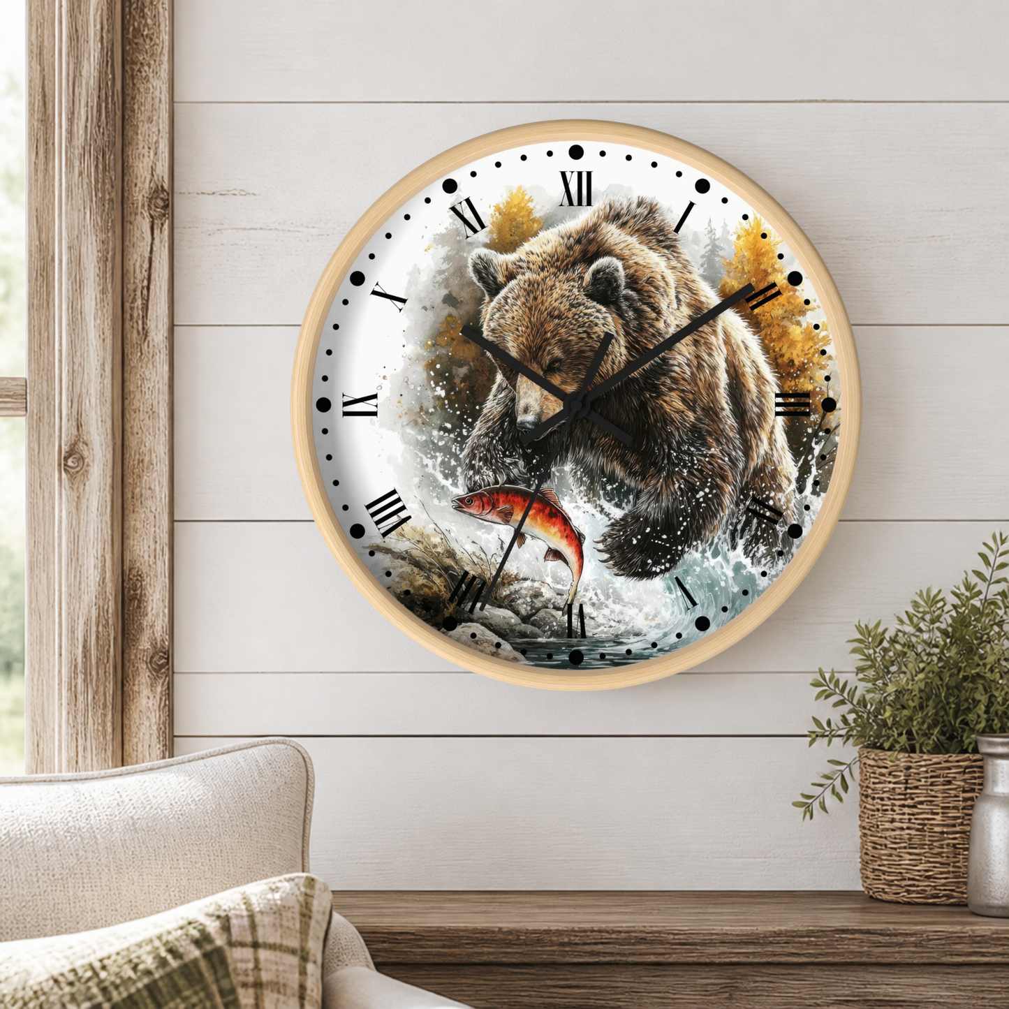 A round wall clock with a light wood frame hangs on a white shiplap wall above a wooden table. The clock face features a detailed illustration of a brown bear catching a red fish, with black Roman numerals and black hands.