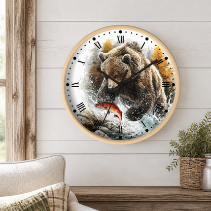 A round wall clock with a light wood frame hangs on a white shiplap wall above a wooden table. The clock face features a detailed illustration of a brown bear catching a red fish, with black Roman numerals and black hands.