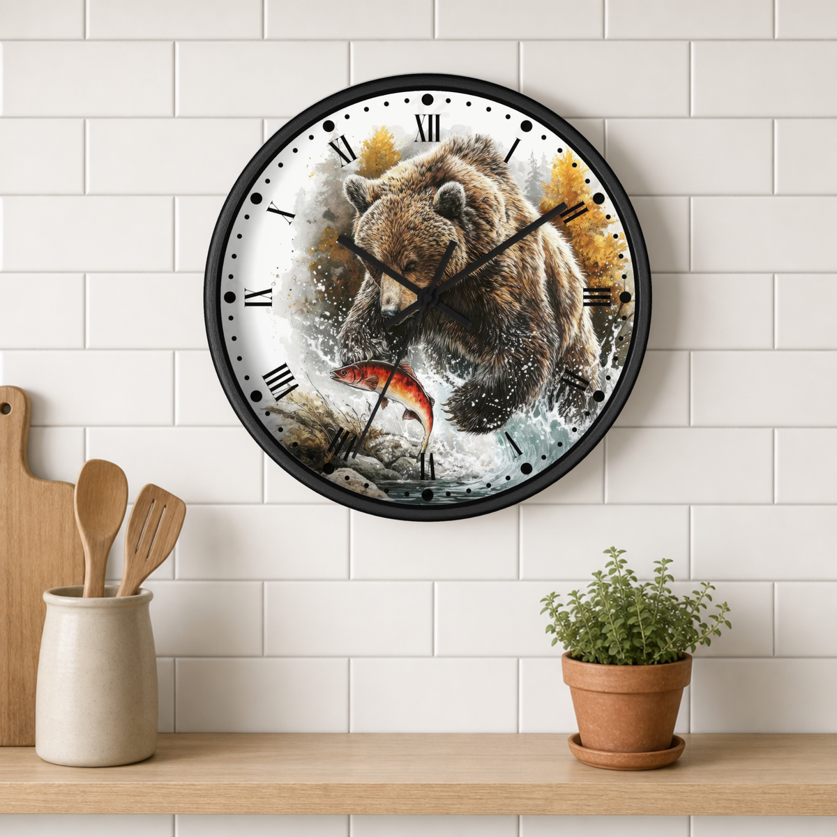 A round wall clock with a black frame hangs on a white subway tile wall above a wooden shelf. The clock face features a detailed illustration of a brown bear catching a red-orange fish, with black Roman numerals and black hands.