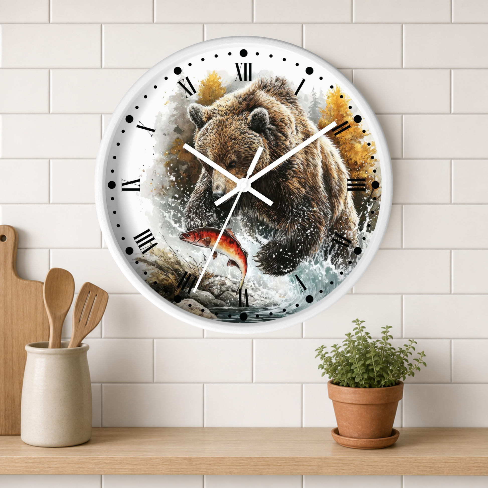 A round wall clock with a white frame and black Roman numerals, featuring a printed illustration of a brown bear catching a red fish in splashing water. The clock is mounted on a white subway tile wall above a wooden shelf with kitchen utensils and a small potted plant.