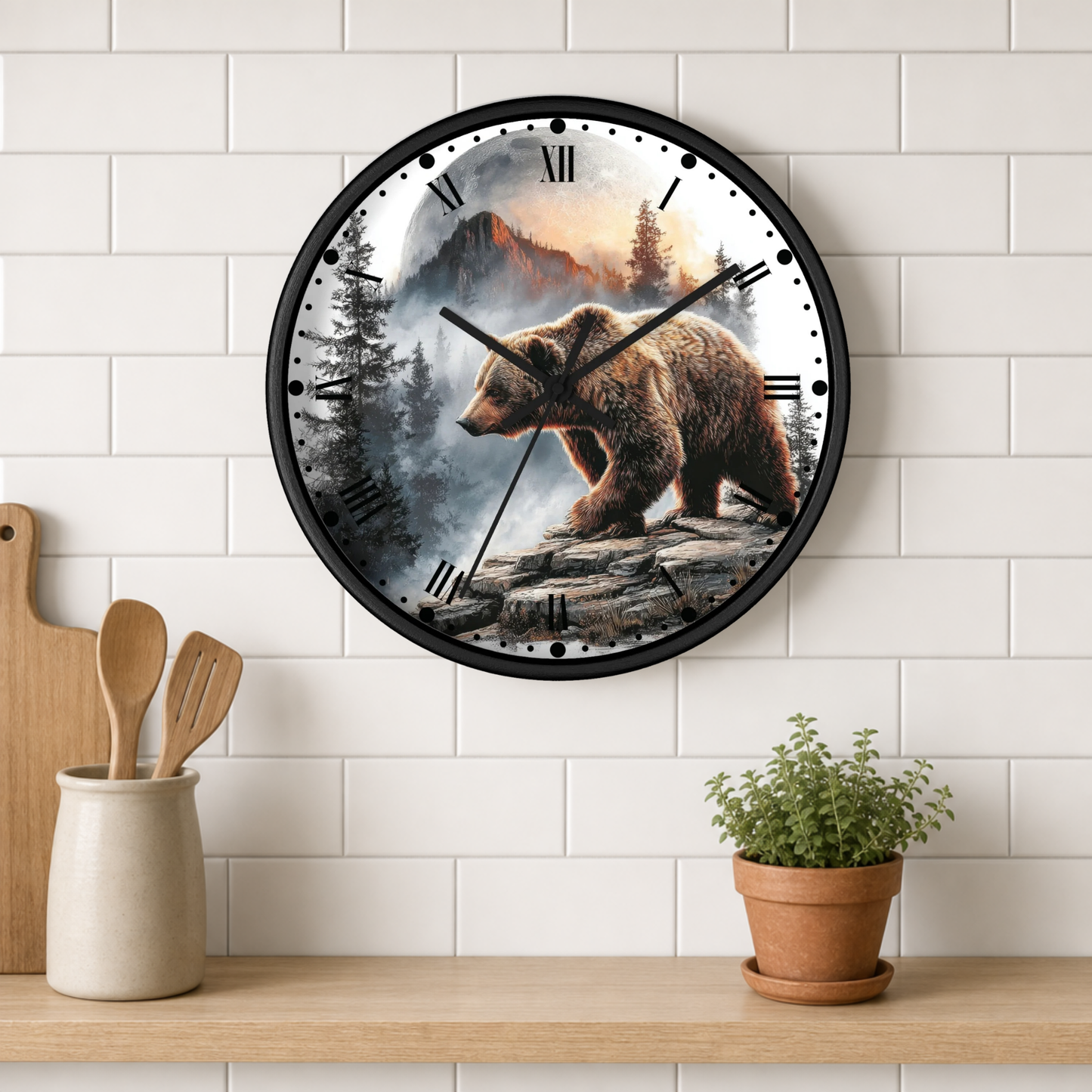 A round wall clock with a black frame and a printed brown bear mountain landscape face, mounted on a white subway tile wall above a wooden shelf with kitchen utensils and a potted plant.