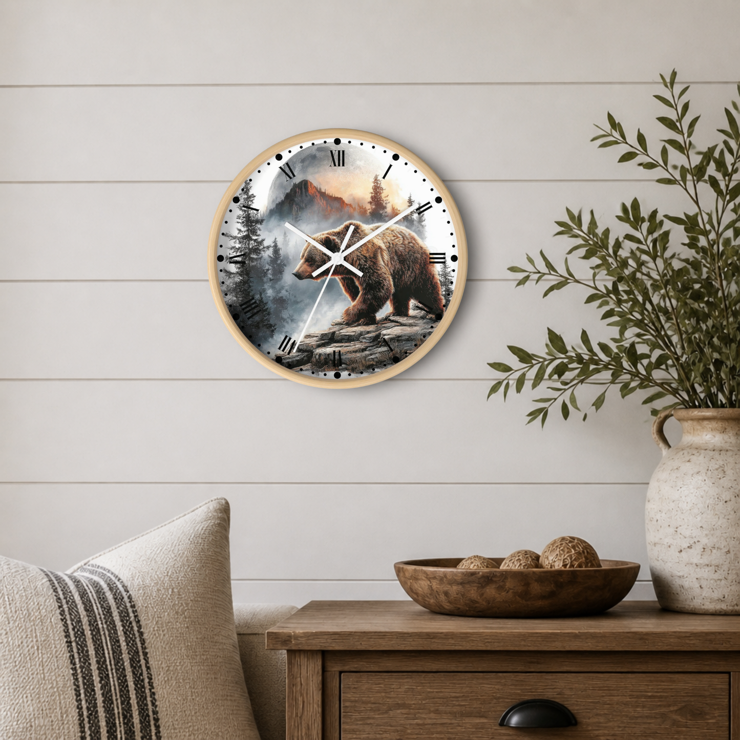 Round wall clock with a natural wood frame and a printed bear hunting scene on the face, mounted on a white shiplap wall above a wooden side table with a plant and decorative bowl.