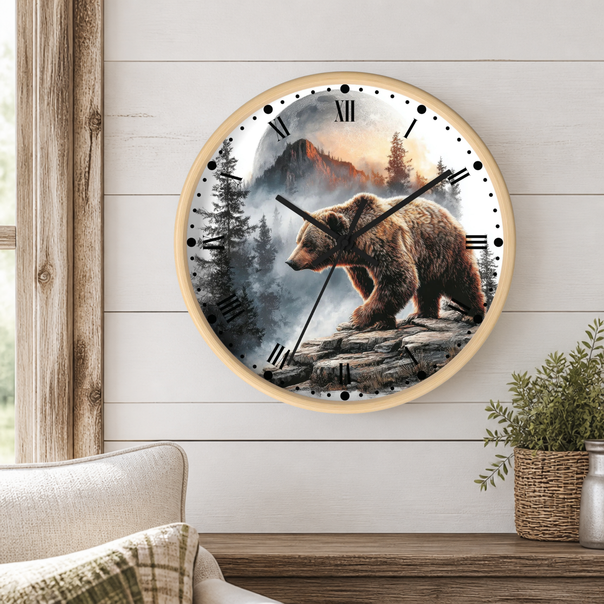 A round wall clock with a light wood frame hangs on a white shiplap wall above a wooden table. The clock face features a detailed graphic of a brown bear walking over rocks in a misty pine forest under a full moon.