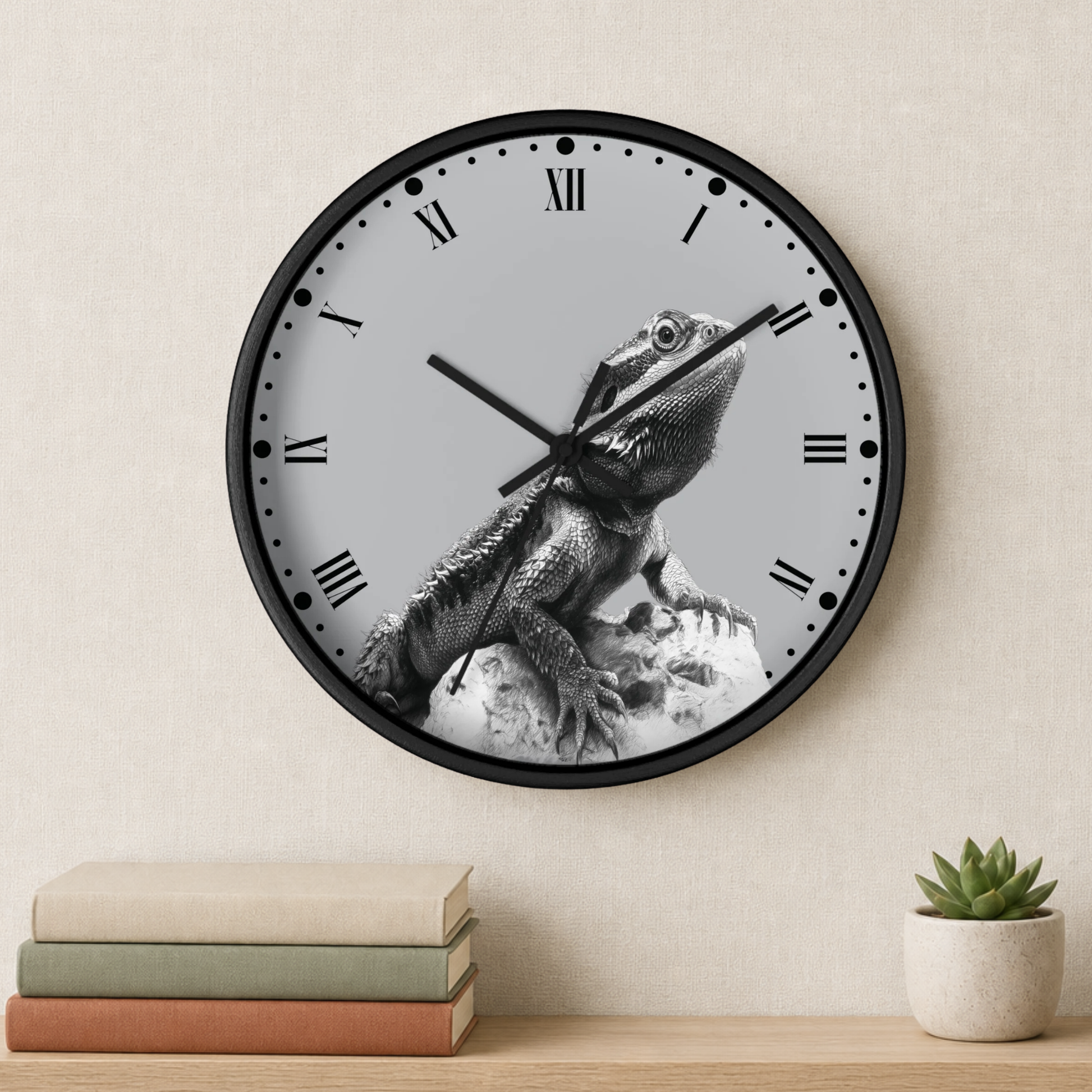 A round wall clock with a black frame and a light gray face featuring a black-and-white photo of a bearded dragon lizard. The clock is mounted on a beige wall above a wooden shelf holding stacked books and a small potted succulent.