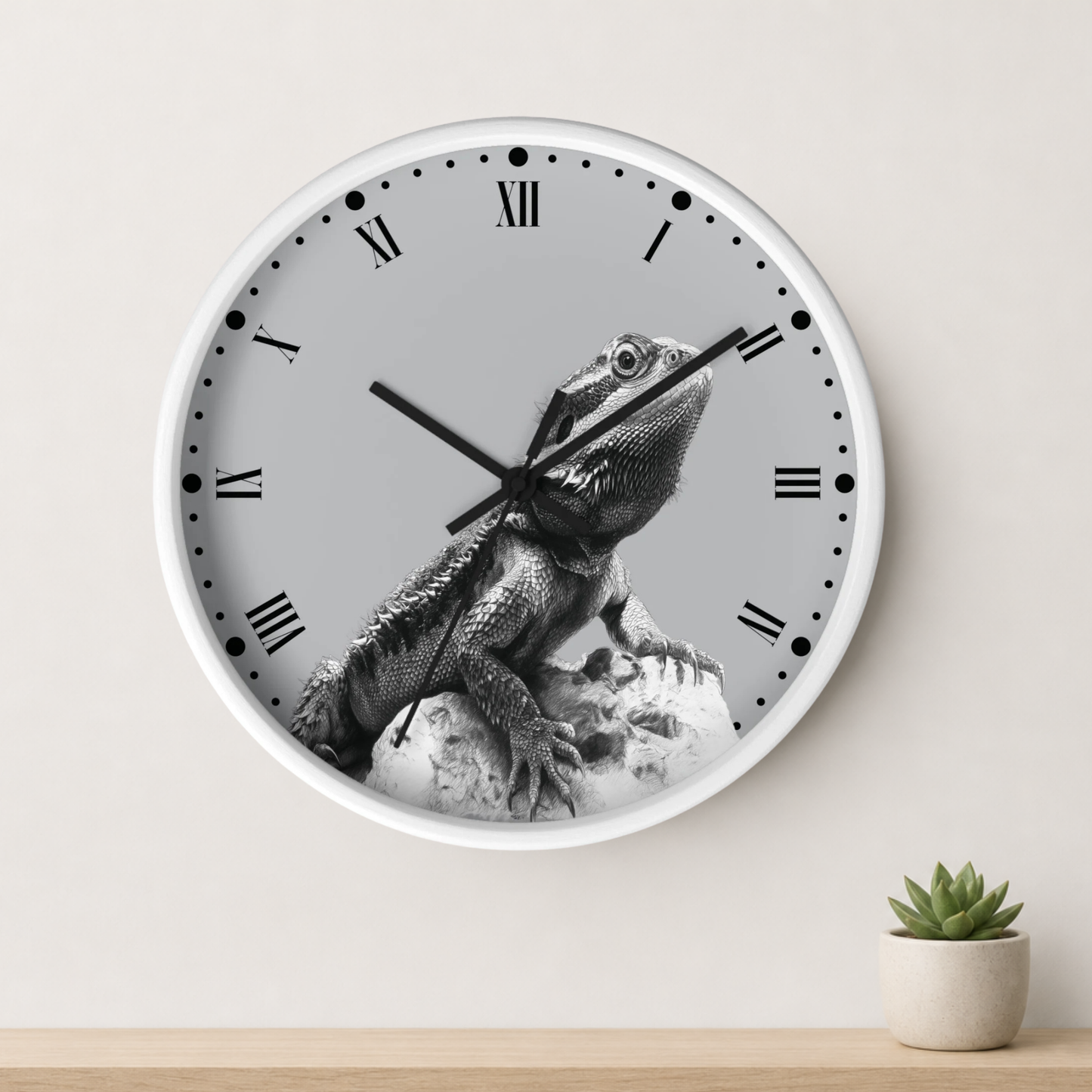 A round wall clock with a white frame and a grayscale lizard graphic on the face, mounted on a light wall above a small potted succulent.