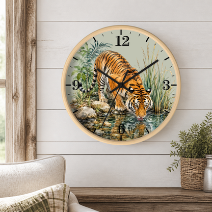 A round wall clock with a light wood frame hangs on a white shiplap wall above a wooden table. The clock face features a detailed illustration of an orange and black tiger drinking water from a stream, surrounded by green foliage.