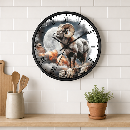 A round wall clock with a black frame and a printed ram illustration over a moon and clouds, mounted on a white subway-tile wall above a wooden shelf with kitchen utensils and a potted plant.