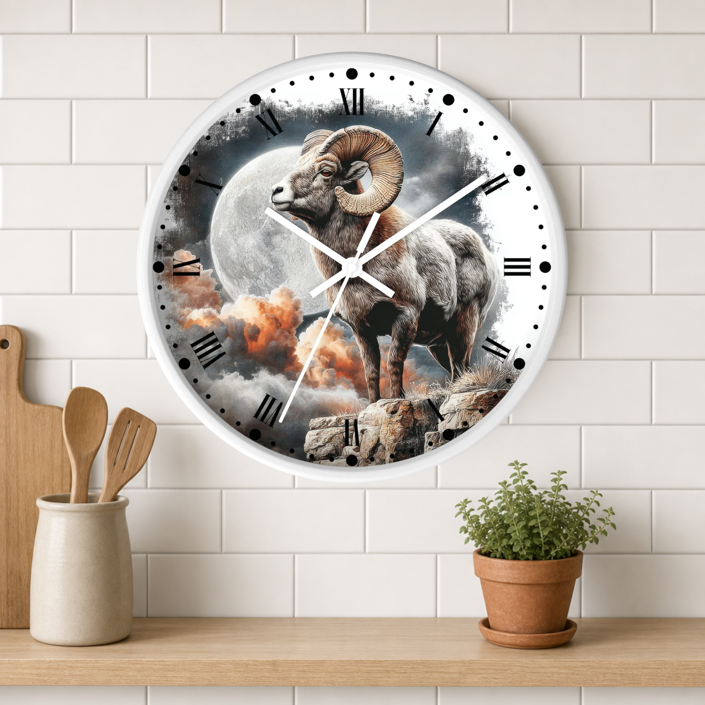 A round wall clock with a white rim and black Roman numerals, featuring a detailed illustration of a ram standing before a large moon and clouds. The clock is mounted on a white subway-tile wall above a wooden shelf with a small potted plant and kitchen utensils.