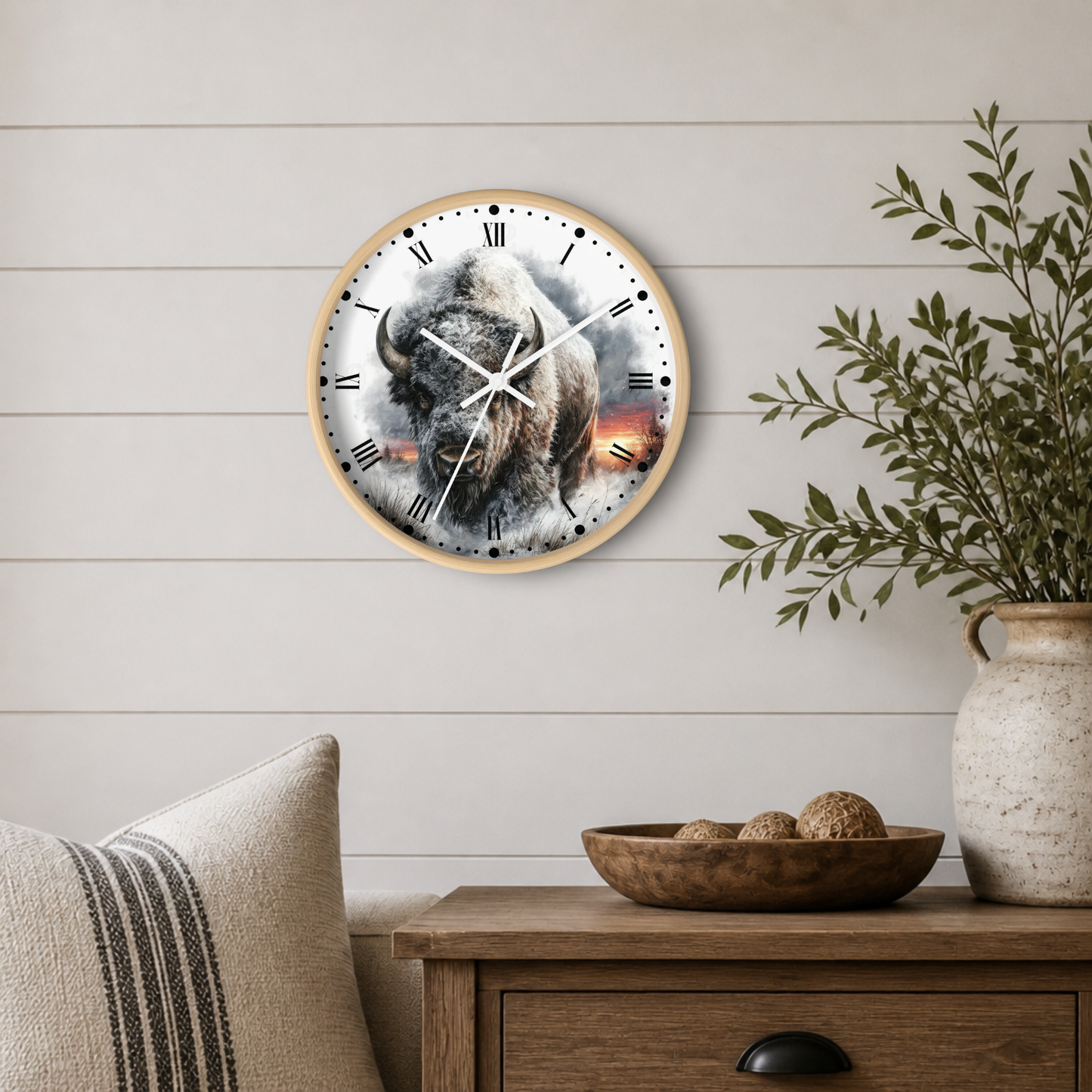 Round wall clock with a natural wood frame and a western bison print on the face, styled on a light wood-paneled wall above a wooden side table with a plant and decorative items.
