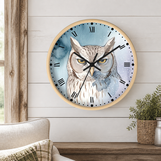 A round wall clock with a light wood frame hangs on a white shiplap wall above a wooden table. The clock face features a detailed watercolor illustration of an owl with yellow eyes against a blue and white background.