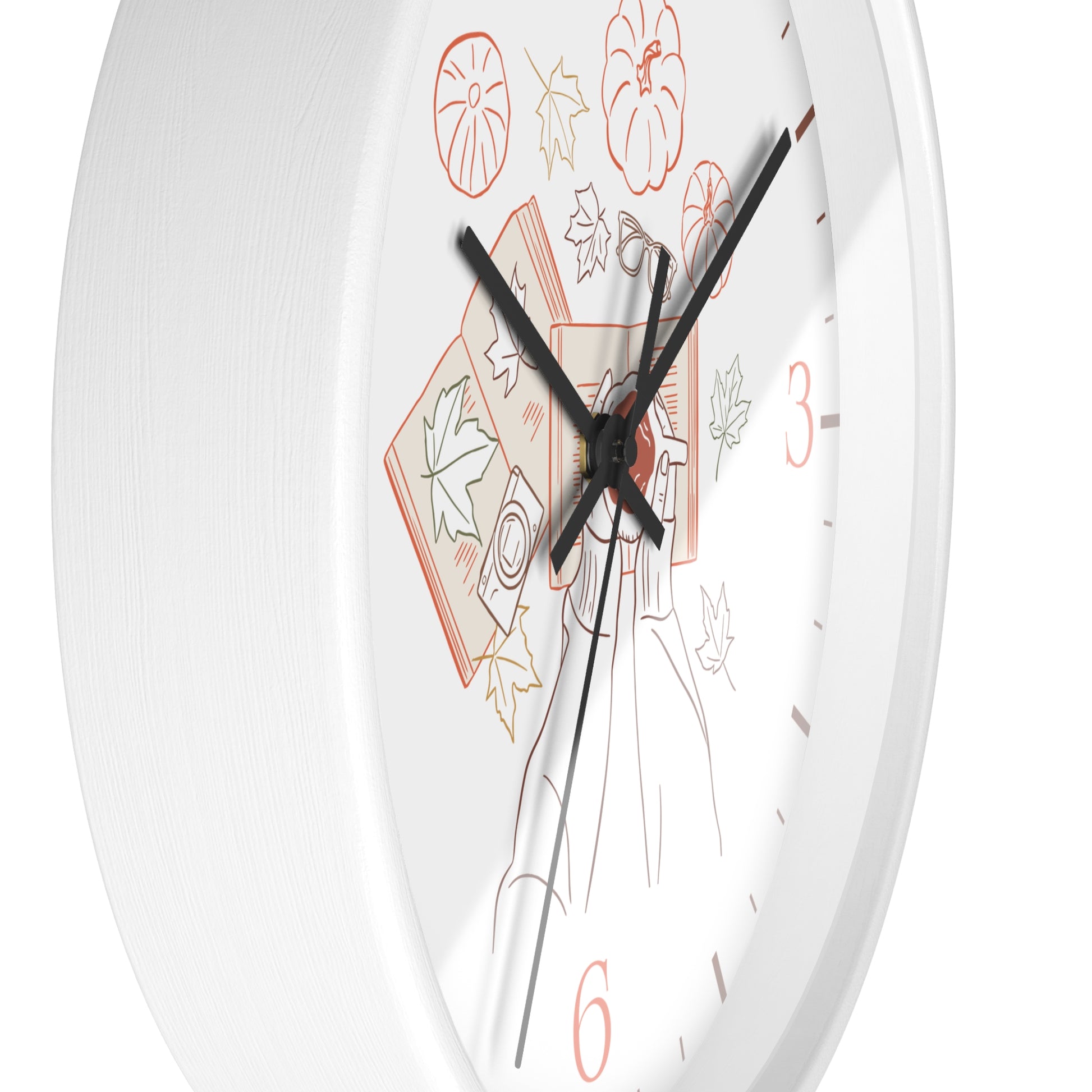 A close-up of a white round wall clock face with black hands and a minimalist autumn-themed illustration featuring orange numerals and leaf motifs.