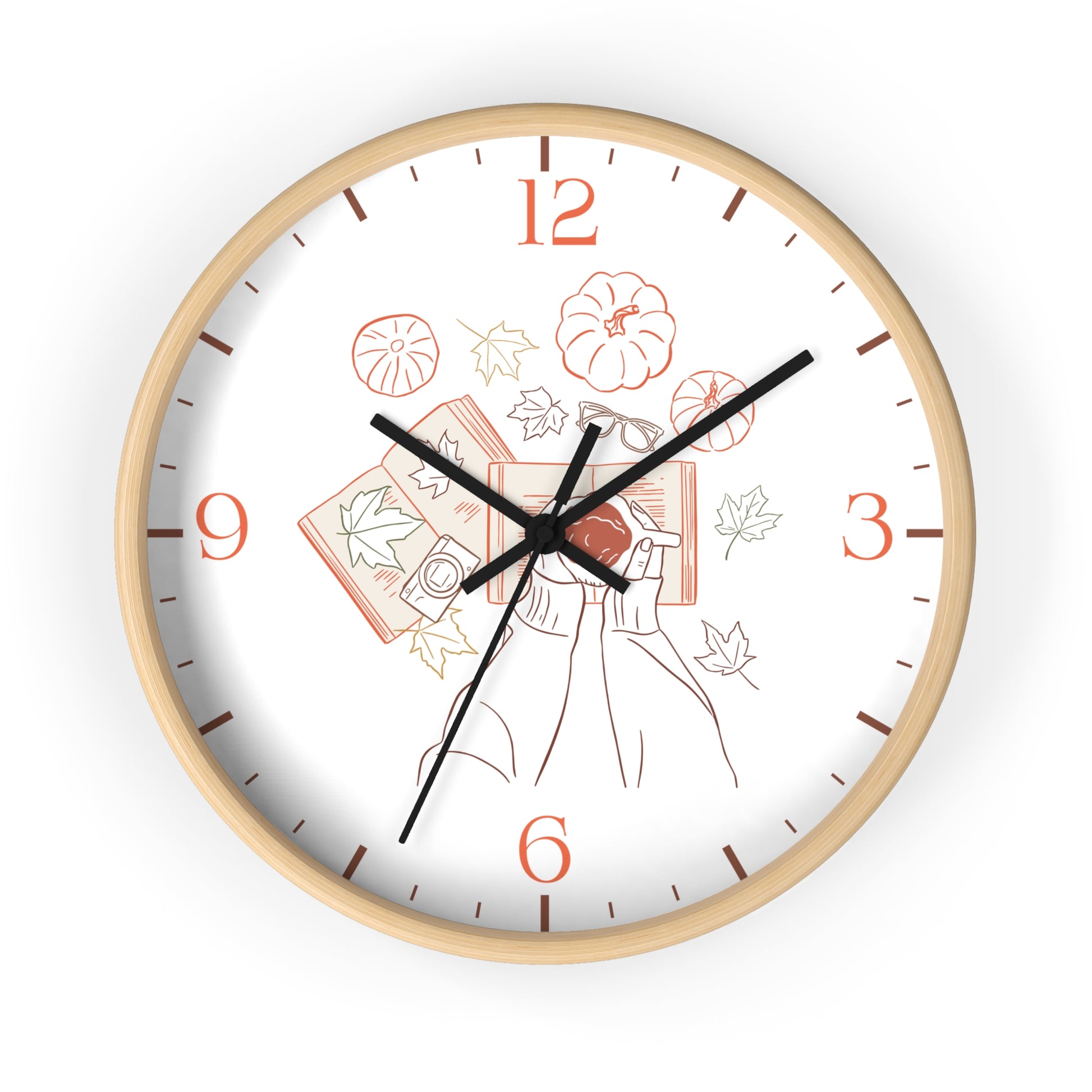 A round wall clock with a light natural wood frame and a white face featuring a minimalist autumn illustration with orange numerals and black hands.