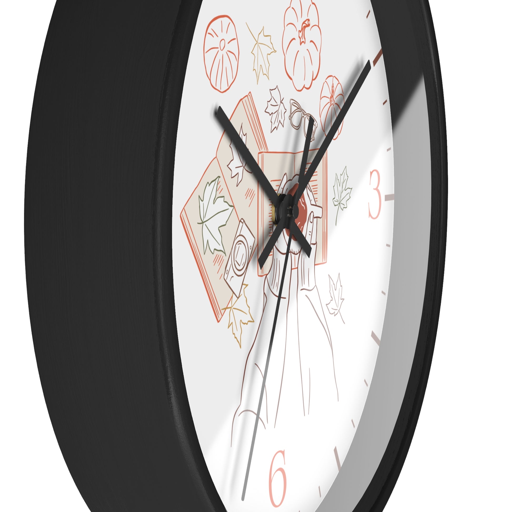 A close-up of a round wall clock with a black frame and a white face featuring autumn-themed line drawings, including pumpkins, leaves, and a figure, with black and red numerals.