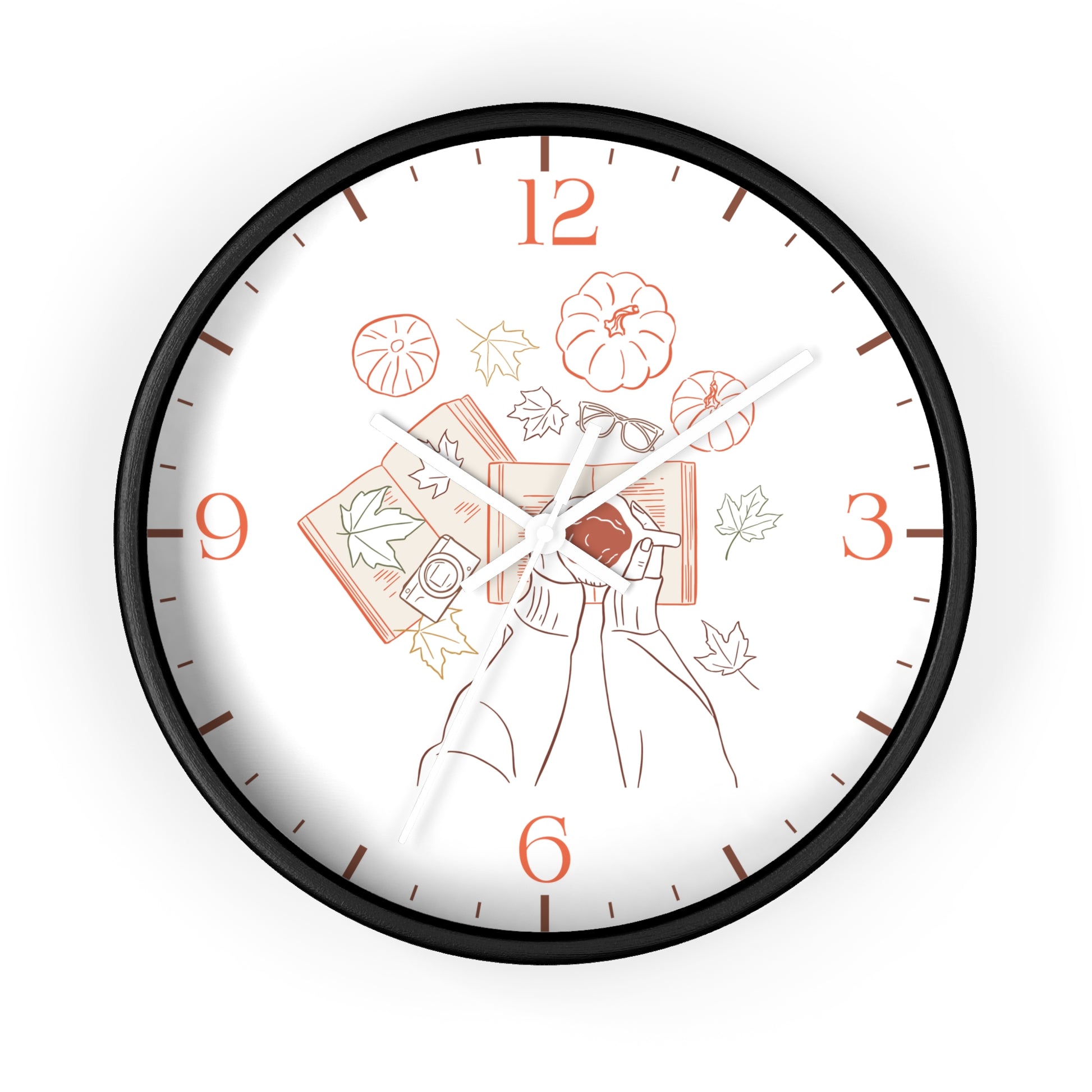 A round wall clock with a black frame and a white face featuring an autumn-themed illustration of a person holding a book, pumpkins, leaves, and orange numerals.