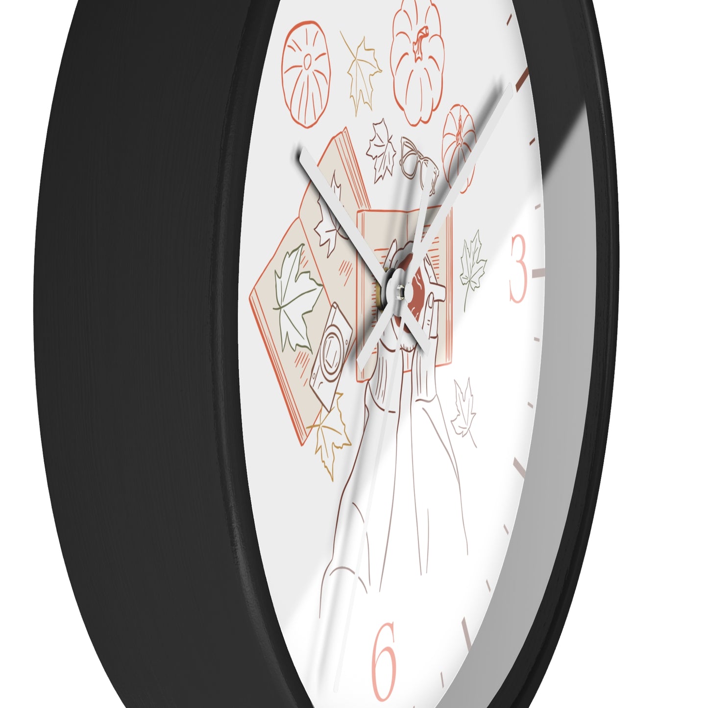 A close-up of a round wall clock with a black frame and a white face featuring autumn-themed line art, including a pumpkin, leaves, a book, and orange numerals.