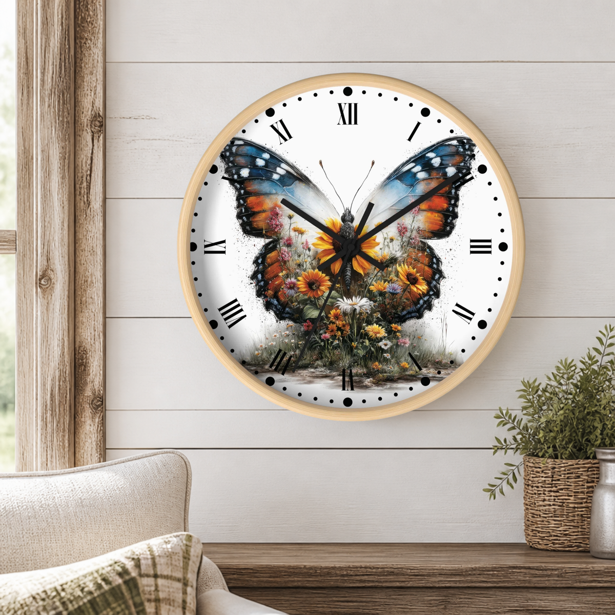 A round wall clock with a light wood frame hangs on a white shiplap wall above a wooden table. The clock face features a large colorful butterfly with orange, blue, and black wings over a field of yellow and white flowers.