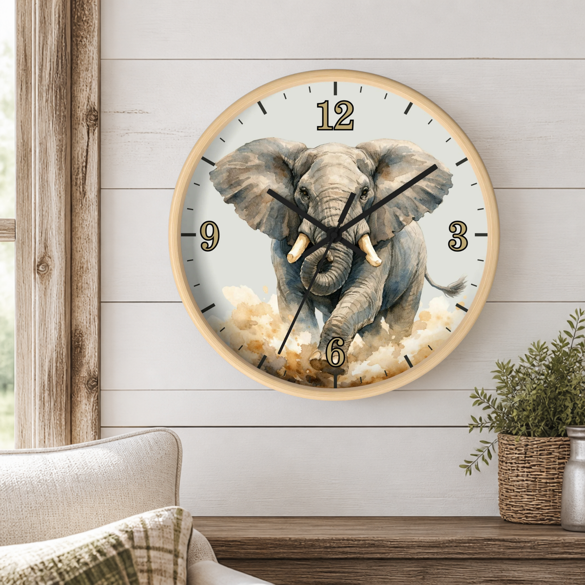 A round wall clock with a light wood frame hangs on a white shiplap wall above a wooden table. The clock face features a detailed illustration of a gray elephant emerging from clouds, with black Arabic numerals and black hands.