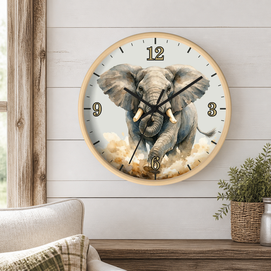 A round wall clock with a light wood frame hangs on a white shiplap wall above a wooden table. The clock face features a detailed illustration of a gray elephant emerging from clouds, with black Arabic numerals and black hands.