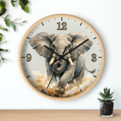 Round wall clock with a light wood frame and a printed elephant design on the face, shown hanging on a white wall above a wooden surface with small green plants nearby.