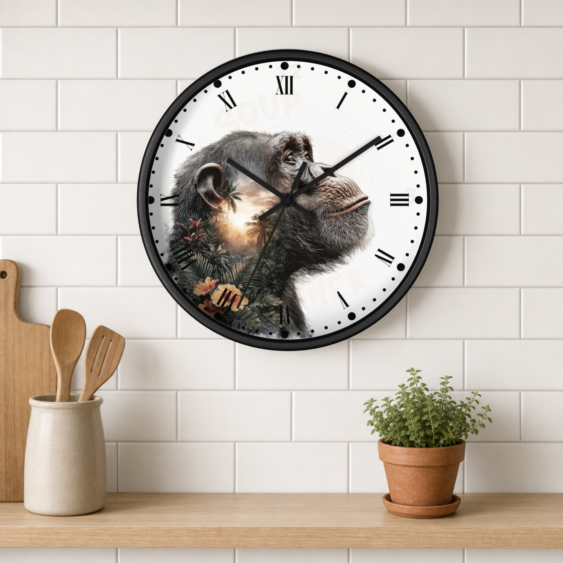 A round wall clock with a black frame and a chimpanzee face printed on the dial, mounted on a white subway-tile wall above a wooden shelf with kitchen utensils and a potted plant.