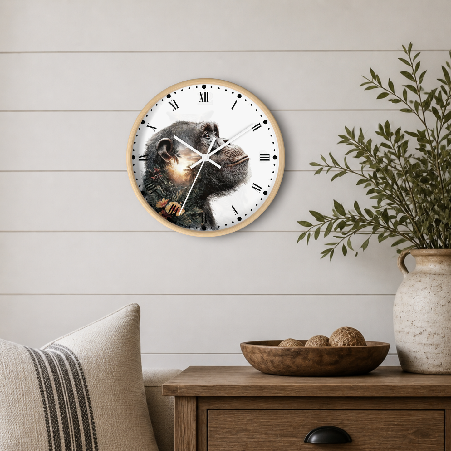 Round wall clock with a chimpanzee face printed on the face, mounted on a white shiplap wall above a wooden side table with a plant and decorative bowl.