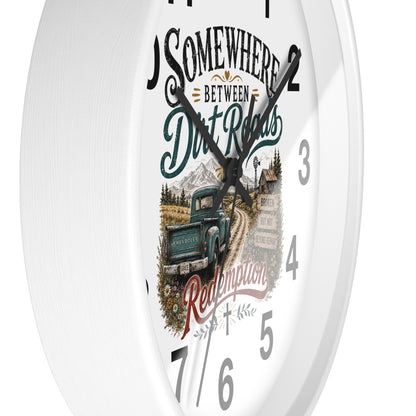 A white round wall clock with a rustic western-themed dial design featuring the text 'Somewhere Between Dirt Roads Redemption' and an illustration of a vintage pickup truck on a dirt road.
