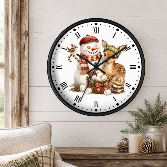 A round wall clock with a black frame and a white face featuring a winter holiday illustration of a snowman and a deer, shown hanging on a light wood-paneled wall above a table with candles and pinecones.