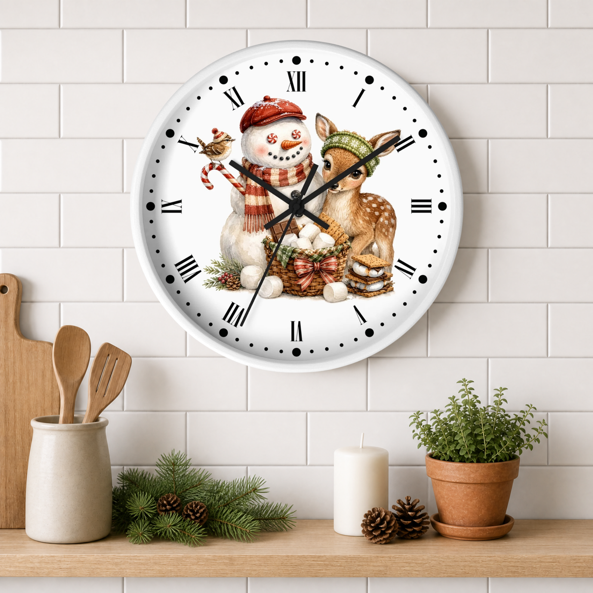 A round wall clock with a white face and black Roman numerals, decorated with a festive illustration of a snowman and a deer in winter clothing. The clock is mounted on a white subway tile wall above a wooden shelf styled with a small potted plant, pinecones, a candle, and wooden utensils.