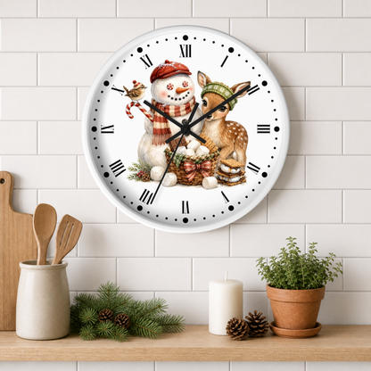 A round wall clock with a white face and black Roman numerals, decorated with a festive illustration of a snowman and a deer in winter clothing. The clock is mounted on a white subway tile wall above a wooden shelf styled with a small potted plant, pinecones, a candle, and wooden utensils.