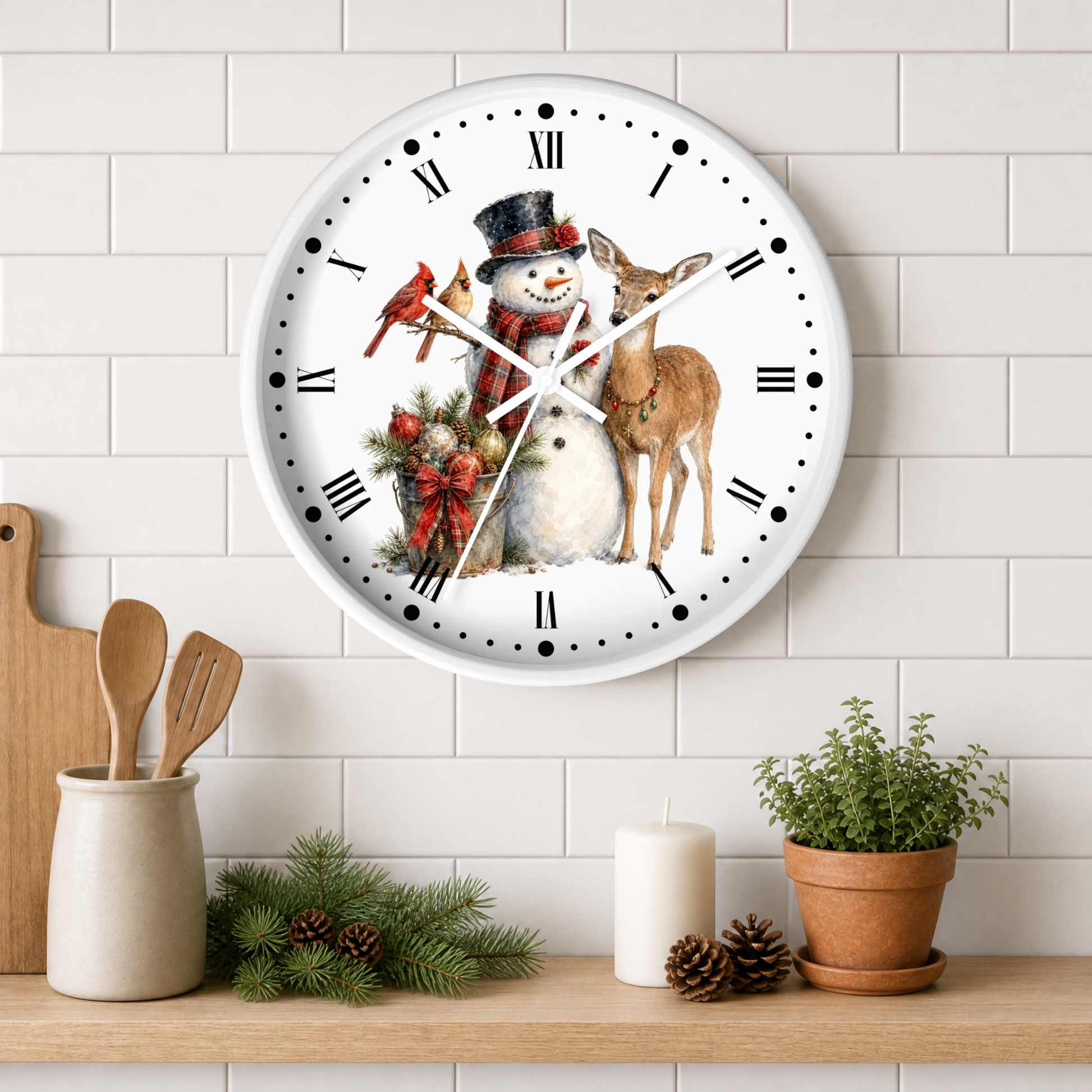 A round white wall clock with a festive Christmas illustration of a snowman, deer, bird, and red cardinal, mounted on a white subway tile wall above a wooden shelf with kitchen decor.