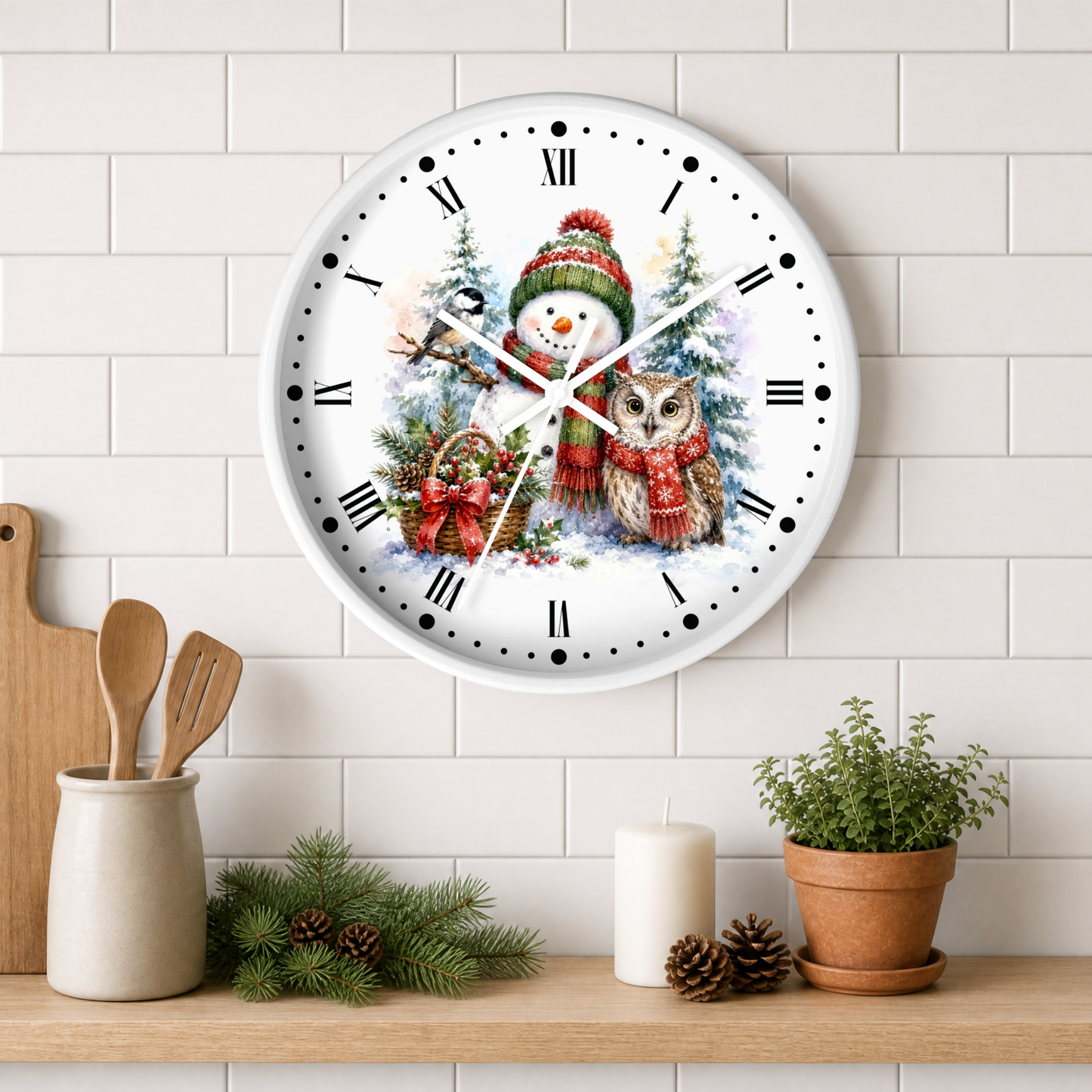 A round white wall clock with a festive winter illustration of a snowman and an owl, mounted on a white subway tile wall above a wooden shelf with kitchen decor and a potted plant.