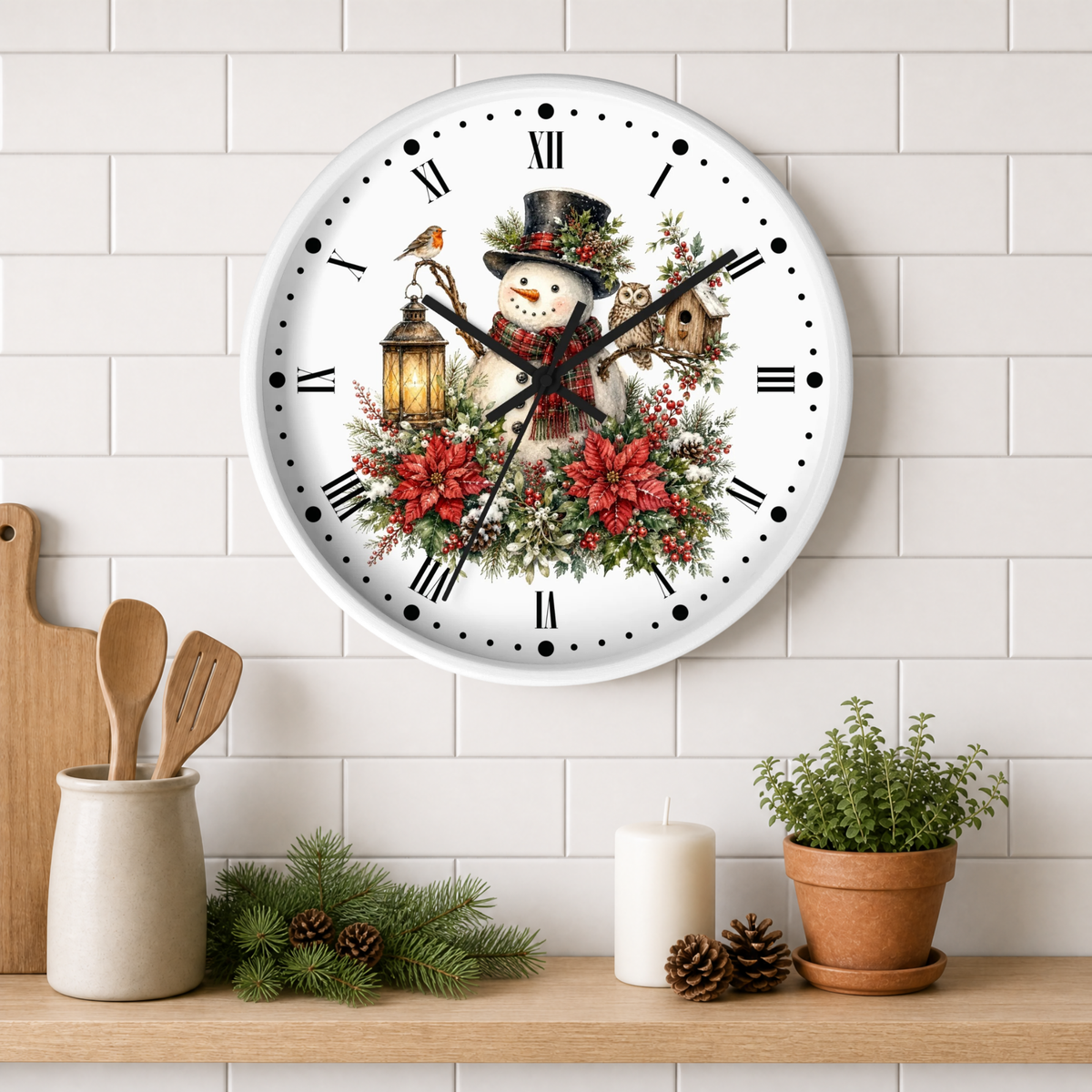A round white wall clock with a festive Christmas design featuring a snowman, red poinsettias, a bird, and a lantern. The clock is mounted on a white subway tile wall above a wooden shelf styled with kitchen utensils, pine branches, a candle, and a potted plant.