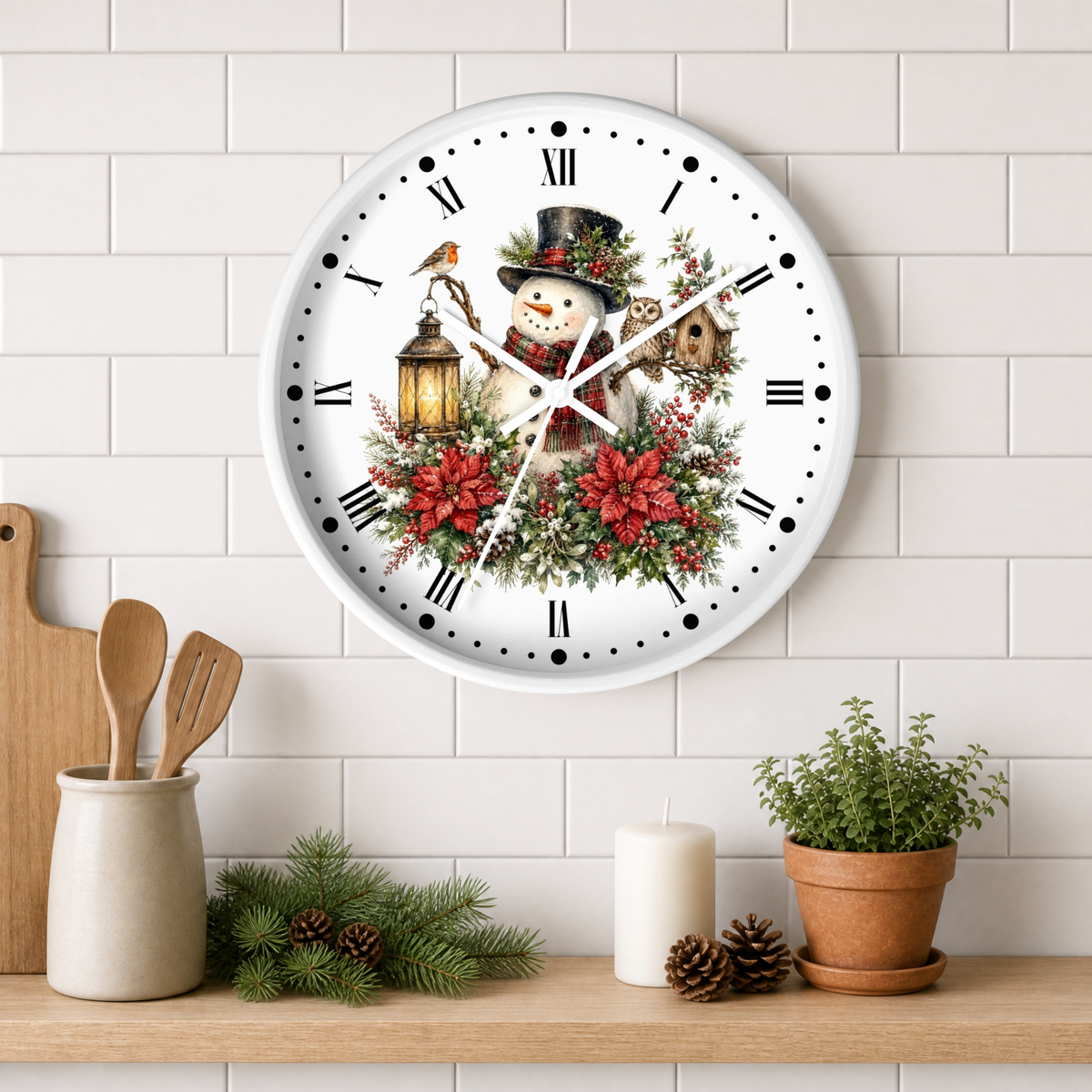 A round white wall clock with a festive winter illustration of a snowman, birds, a lantern, and red poinsettias, mounted on a white subway tile wall above a wooden shelf with kitchen decor and a potted plant.