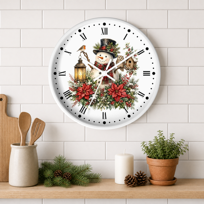A round white wall clock with a festive winter illustration of a snowman, birds, a lantern, and red poinsettias, mounted on a white subway tile wall above a wooden shelf with kitchen decor and a potted plant.