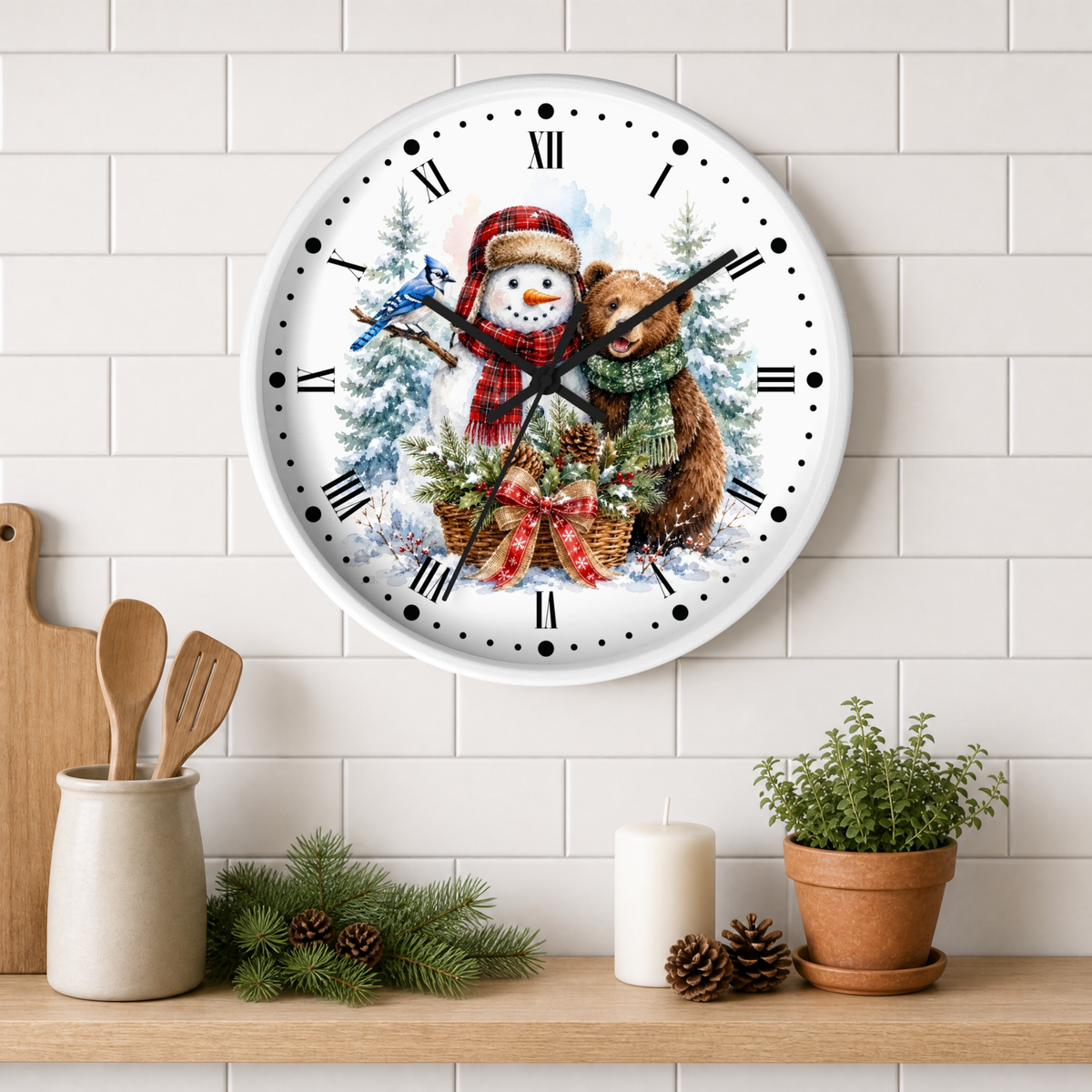 A round wall clock with a festive Christmas illustration of a snowman, a bear, pine trees, and holiday gifts, mounted on a white subway tile wall above a wooden shelf with kitchen decor.