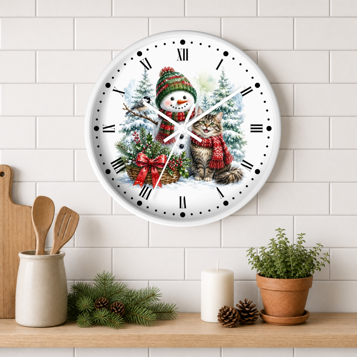 A round wall clock with a white face and black Roman numerals, featuring a festive Christmas illustration of a snowman and a cat. The clock is mounted on a white subway tile wall above a wooden shelf styled with kitchen utensils, pine branches, a candle, and a potted plant.