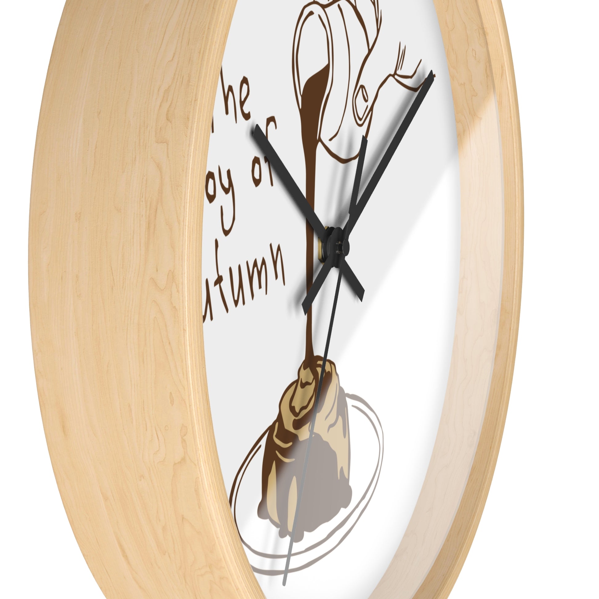 Close-up of a round wall clock with a light natural wood frame and a white face featuring a brown illustration of a pastry and dripping chocolate, with partial text reading 'The joy of autumn'.