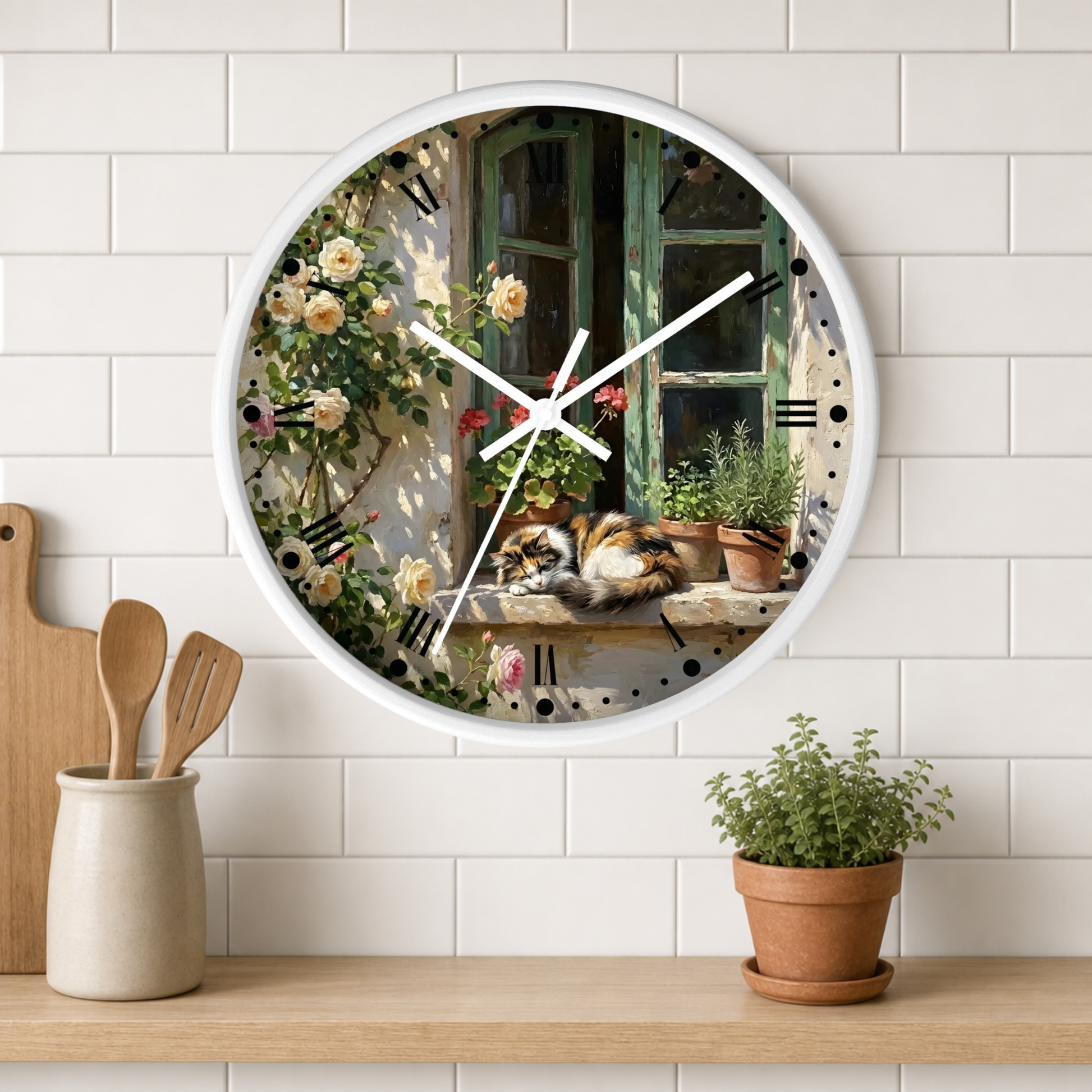 A round wall clock with a white frame hangs on a white subway-tile wall above a wooden shelf. The clock face features a detailed painting of a cat sleeping on a windowsill surrounded by flowers and potted plants.