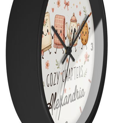 A close-up of a round wall clock with a black frame and a white face featuring cute illustrated characters and the text 'COZY CHAPTERS' and 'Alexandria'.