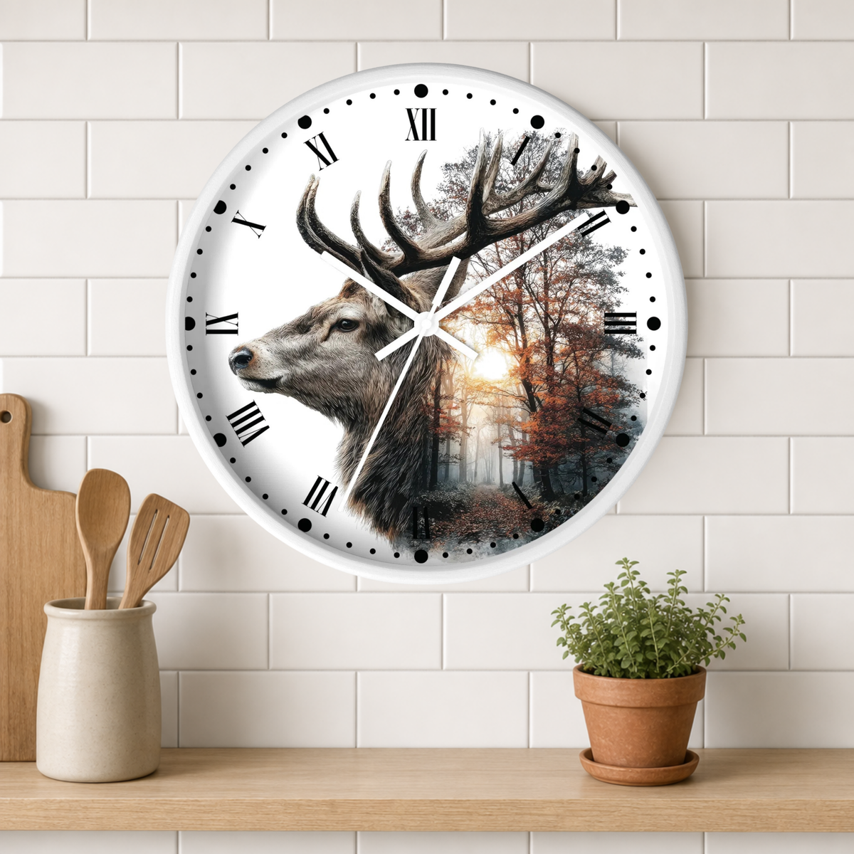 A round wall clock with a white frame and black Roman numerals, featuring a deer head and forest scene printed on the face. The clock is mounted on a white subway tile wall above a wooden shelf with a small potted plant and wooden utensils.