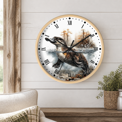 A round wall clock with a light wood frame and a detailed illustration of a duckbill platypus jumping from water, mounted on a white shiplap wall above a wooden table with a plant.