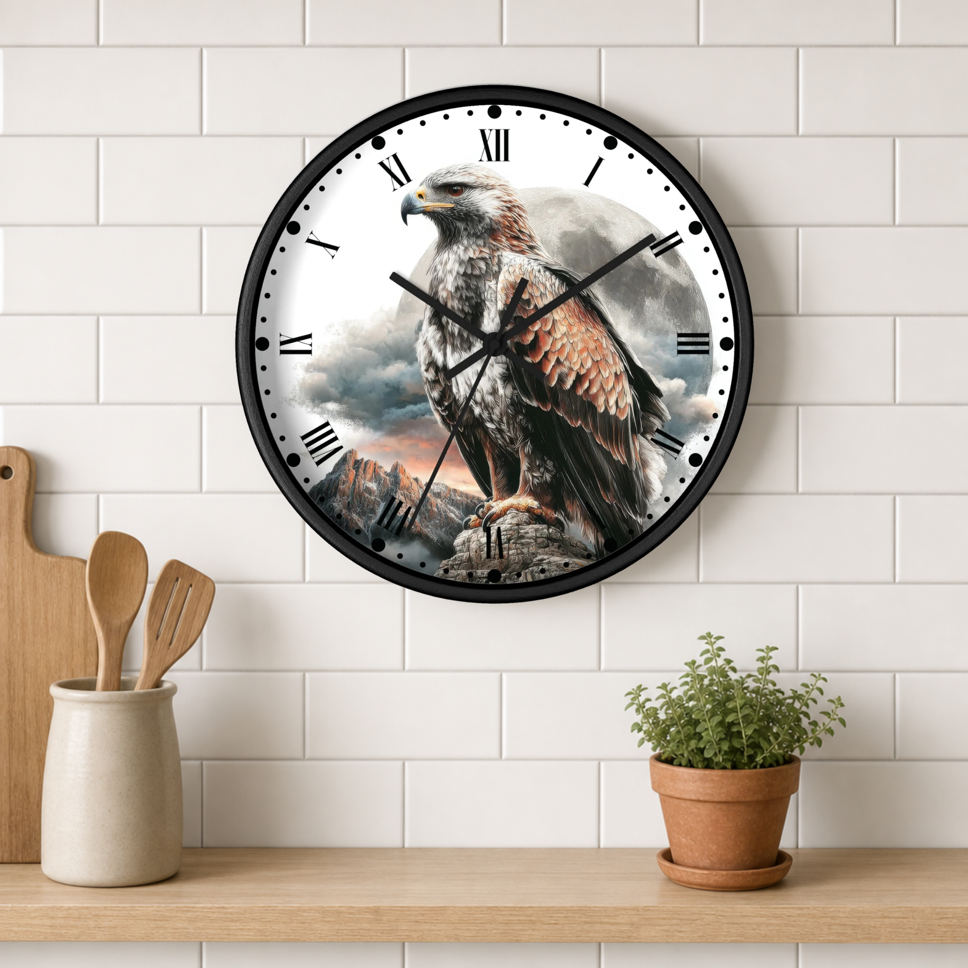 A round wall clock with a black frame and a printed design of a large eagle perched on a rock against a cloudy sky, mounted on a white subway-tile wall above a wooden shelf with kitchen utensils and a small potted plant.