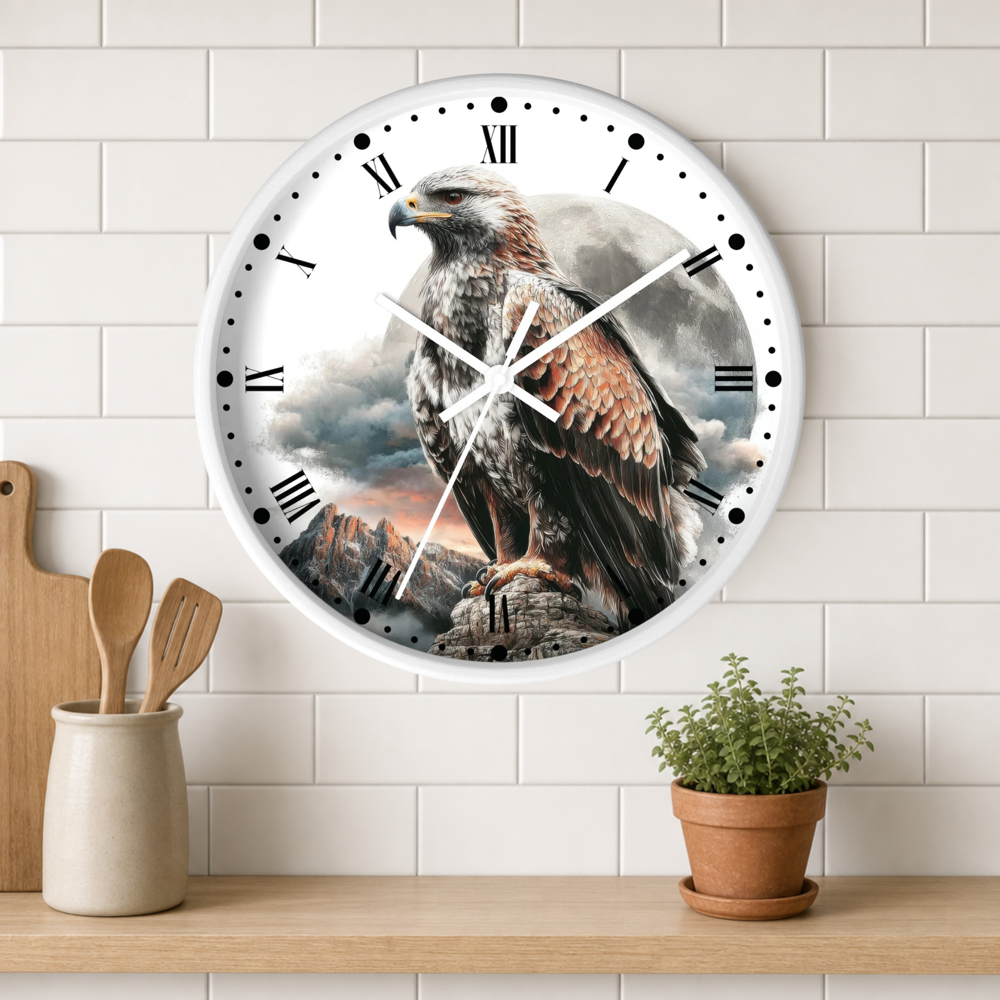 A round wall clock with a white frame and black Roman numerals, featuring a detailed print of a brown and white bird of prey perched on a rocky cliff under a cloudy sky. The clock is mounted on a white subway tile wall above a wooden shelf with kitchen utensils and a small potted plant.