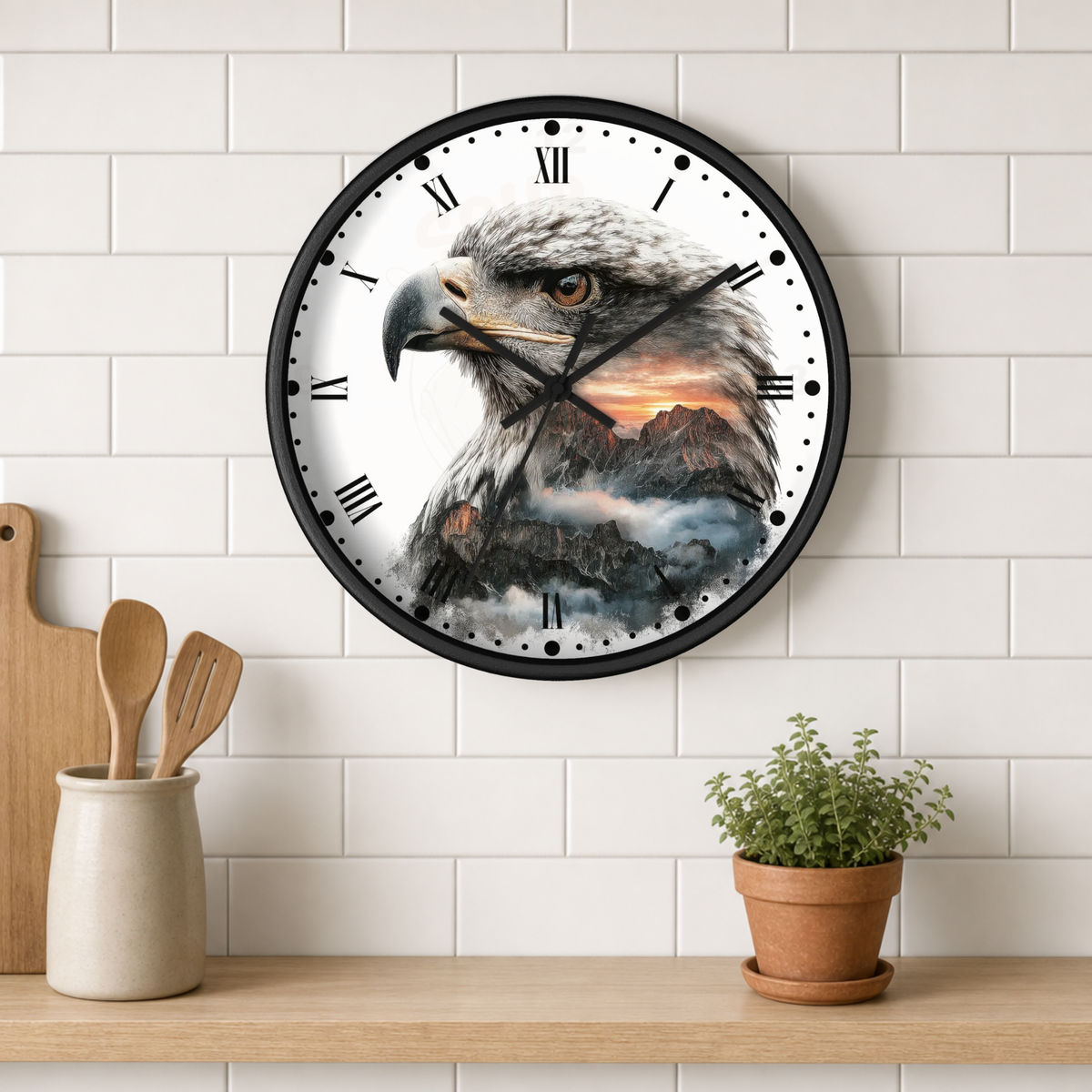 A round wall clock with a black frame and a printed design of a bald eagle over mountains and clouds, mounted on a white subway tile wall above a wooden shelf with kitchen utensils and a potted plant.