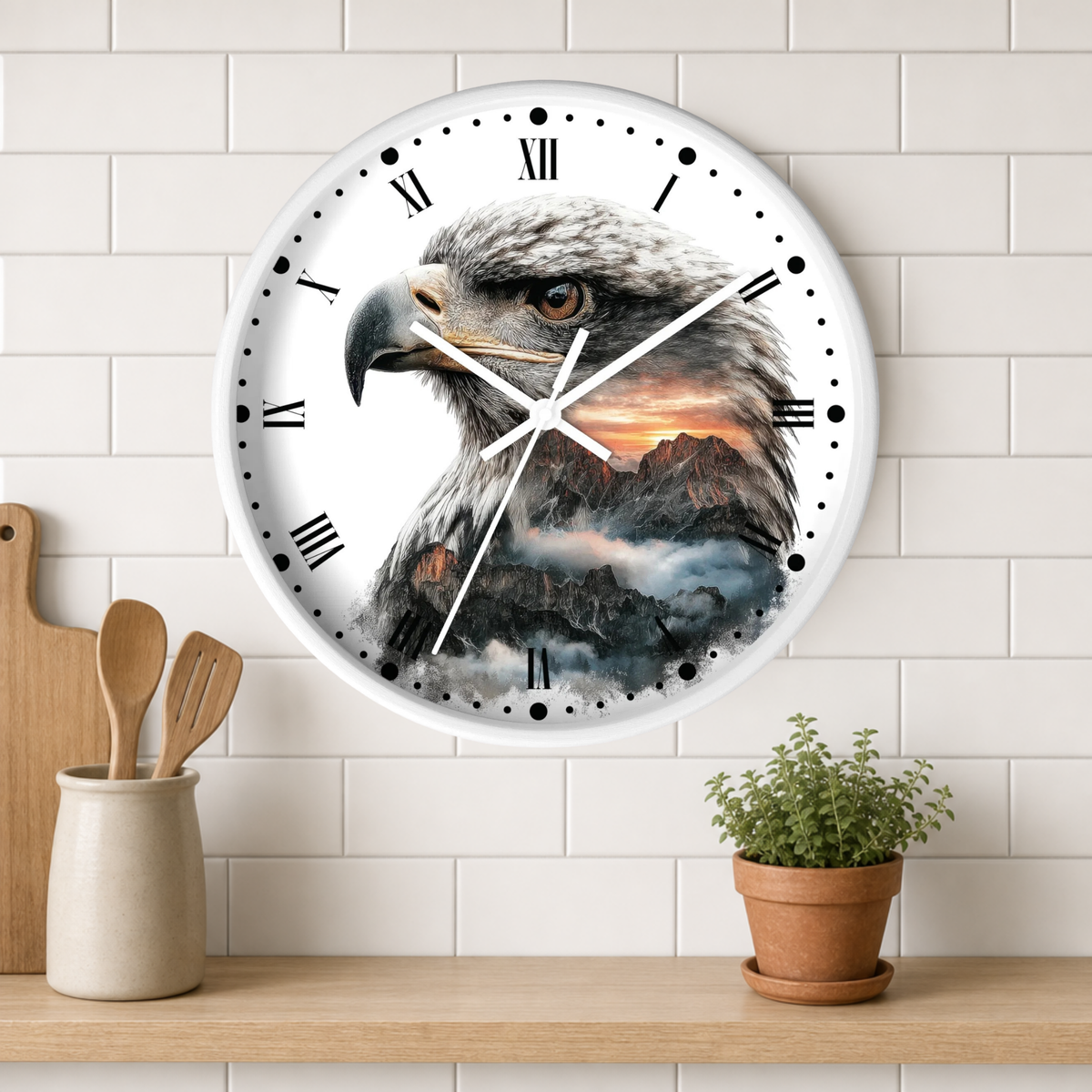 A round wall clock with a white face and Roman numerals, featuring a detailed illustration of an eagle over a mountain landscape. The clock is mounted on a white subway tile wall above a wooden shelf with a small potted plant and wooden utensils.