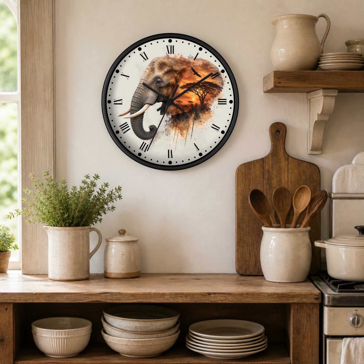 A round wall clock with a black frame and a printed elephant illustration on the face, hanging on a beige wall in a rustic kitchen setting with wooden shelves, ceramic dishes, and plants.