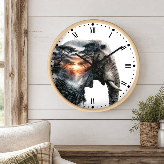 A round wall clock with a light wood frame hangs on a white shiplap wall above a wooden table. The clock face is white with black Roman numerals and hands, featuring a large elephant silhouette filled with a scenic sunset landscape print.